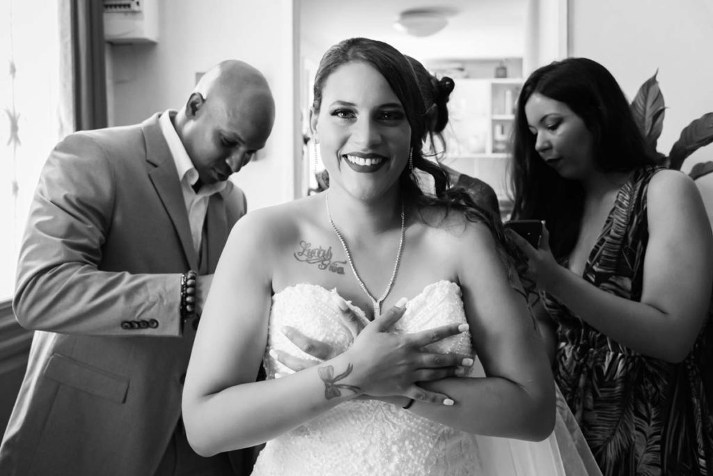 Préparatifs de la mariée qui est en train de mettre sa robe de mariée avec l'aide de ses proches.