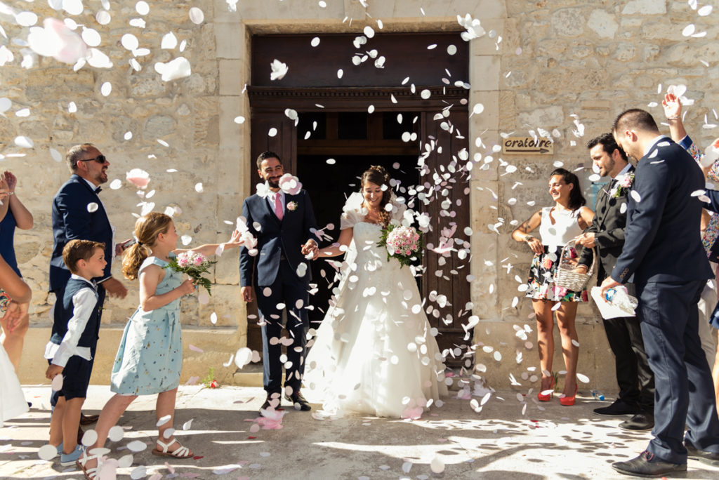 Sortie d'église sous les confettis devant les invités avec une robe de mariée et un costume de marié