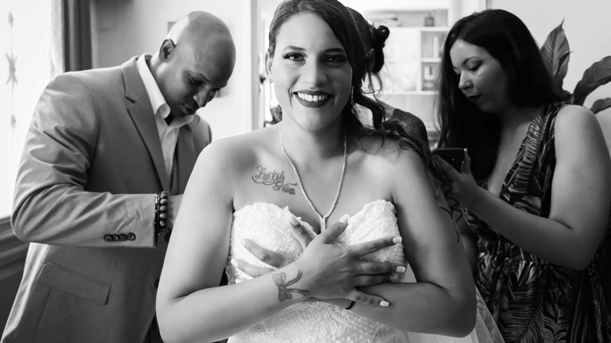 Préparatifs de la mariée qui est en train de mettre sa robe de mariée avec l'aide de ses proches.